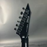Close-up of a black electric guitar headstock with brand logos on a gray background