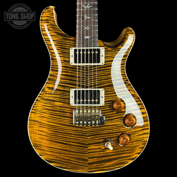 A close-up studio shot of an electric guitar body against a black background, showing a bright yellow-orange flamed maple wood finish with natural wood grain, white pickguard, and hardware.