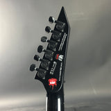 Close-up of a black electric guitar headstock with brand logos on a gray background