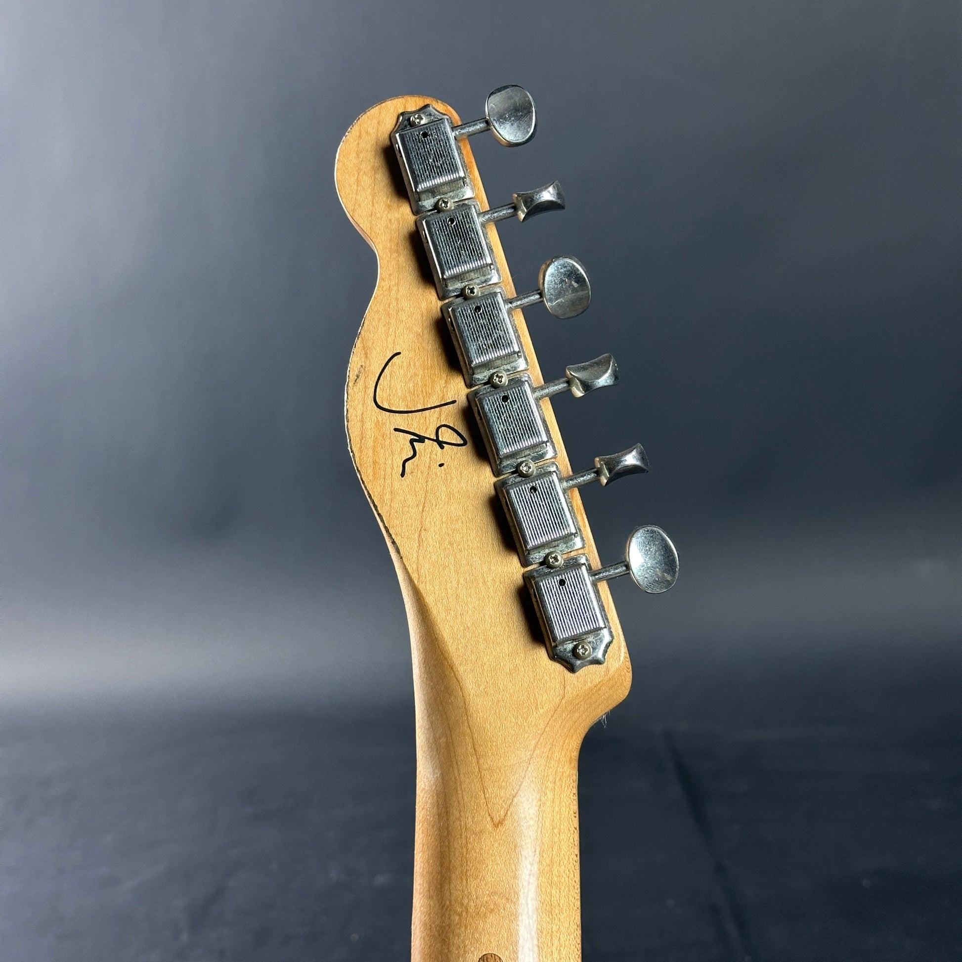 Close-up of a guitar neck with tuning pegs against a dark background