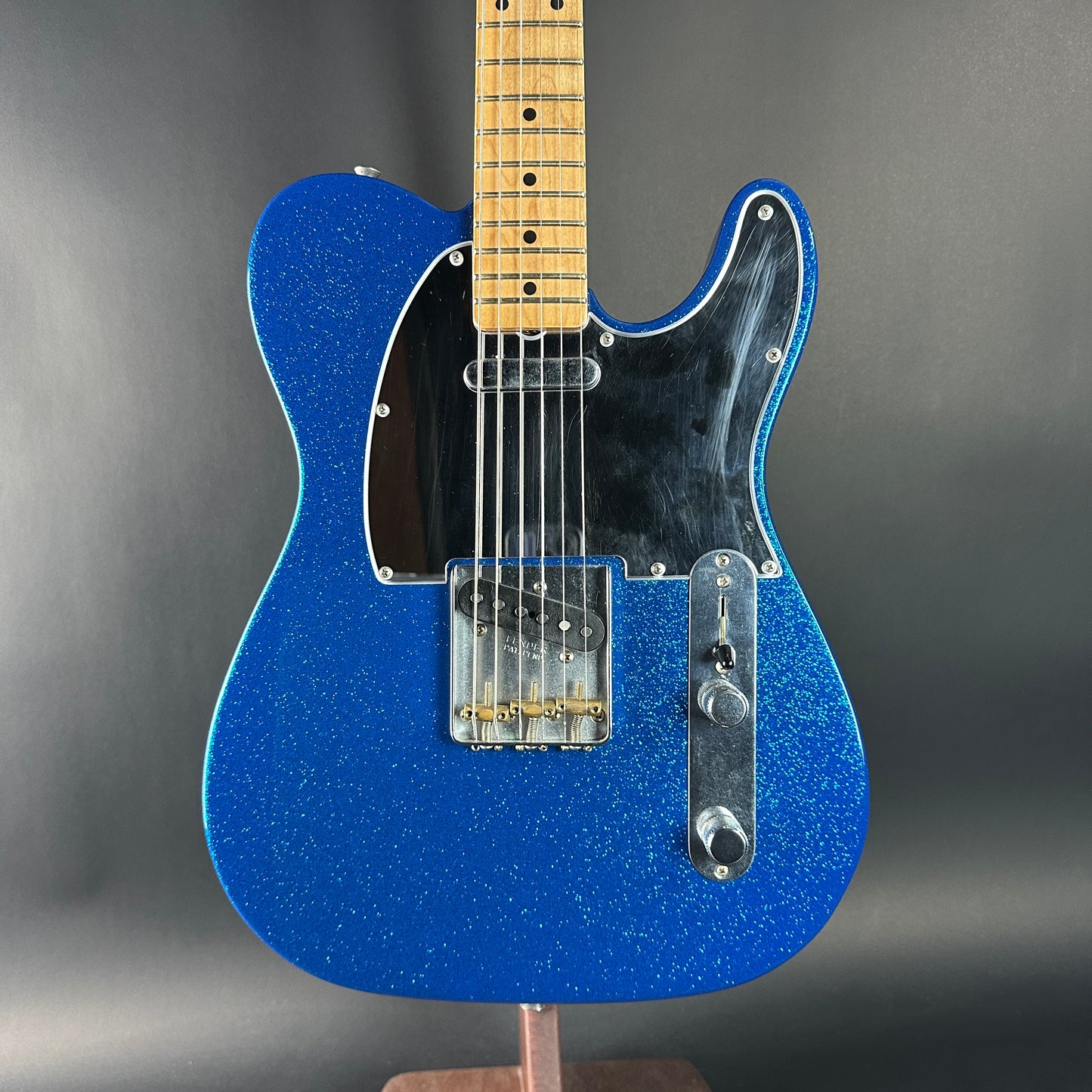 Blue electric guitar with a black pickguard on a gray background