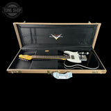 A black electric guitar with a white pickguard and gold headstock, displayed inside an open vintage-style hard case with a black interior and gold trim. A light blue face mask is attached to the front of the case.