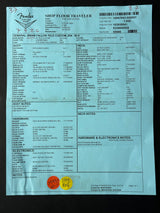 A white paper shipping and receiving document labeled 'SHOP FLOOR TRAVELER' with printed tables, barcodes, and handwritten orange and yellow stamps, photographed against a black background.