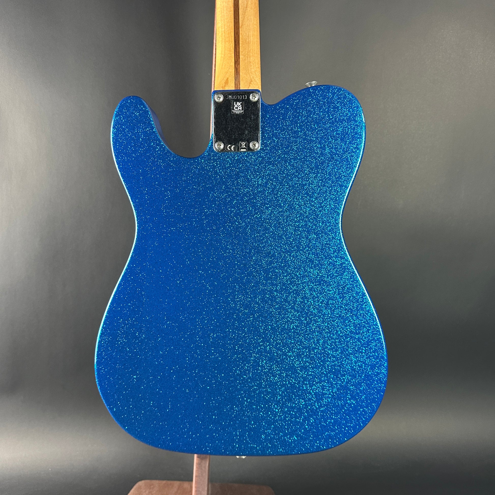 Blue glittery guitar body on a stand with a gray background