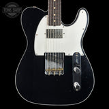 A black electric guitar with a white pickguard, featuring a dark fretboard and gold-toned hardware, shown against a solid black background with a Tone Shop watermark in the top-left corner.
