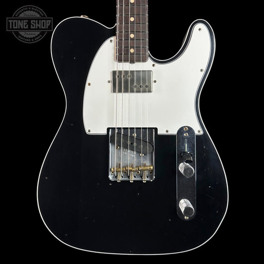 A black electric guitar with a white pickguard, featuring a dark fretboard and gold-toned hardware, shown against a solid black background with a Tone Shop watermark in the top-left corner.