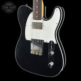 A black electric guitar with a white pickguard, chrome hardware, and a dark fretboard, shown against a black background with a Tone Shop watermark in the top left corner.