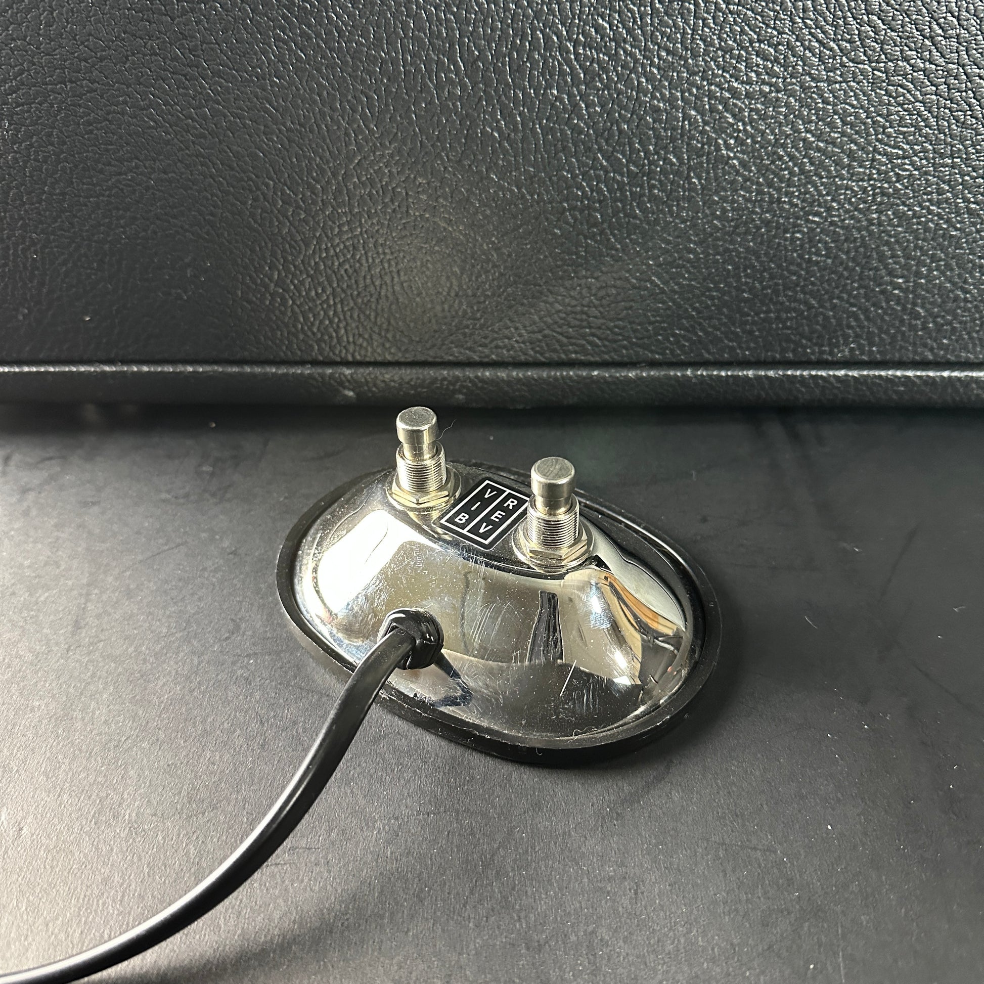 Close-up of a guitar amplifier footswitch with a cable plugged in, on a black surface.