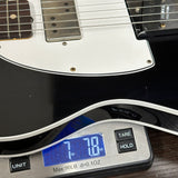 Close-up of a black and white electric guitar body resting on a digital scale displaying 7.78 oz.