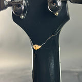 Close-up of the headstock and neck of a black electric guitar, showing a visible crack on the glossy black finish near the tuning pegs.