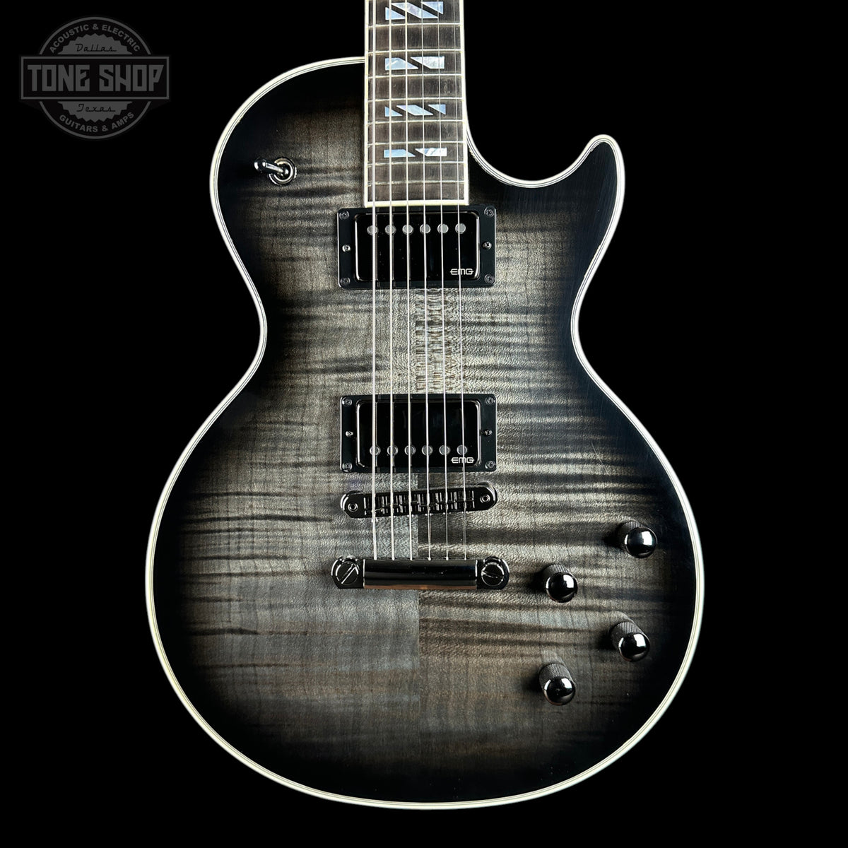 A close-up studio shot of an electric guitar body against a black background, showing a dark gray to black flamed maple wood finish with white binding and chrome hardware. A Tone Shop watermark is visible in the top-left corner.