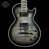 A close-up studio shot of an electric guitar body against a black background, showing a dark gray to black flamed maple wood finish with white binding and chrome hardware. A Tone Shop watermark is visible in the top-left corner.
