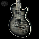 A close-up of an electric guitar body with a dark gray to black woodgrain finish, featuring white binding, dual humbucker pickups, and a control plate with six knobs, shown against a solid black background.