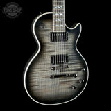 A close-up of an electric guitar body with a dark gray to black flamed maple wood finish, featuring white binding and chrome hardware, set against a solid black background.