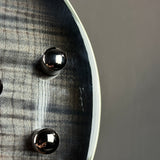 Close-up detail of a guitar body showing a silver flamed maple wood pattern, a white edge trim, and two shiny black hardware knobs against a dark gray background.