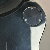 Close-up of a glossy black guitar body with a circular metal hardware detail and visible surface scratches.