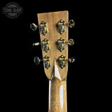 Close-up of the headstock of a wooden acoustic guitar against a solid black background, showing six tuning pegs and a natural wood finish.