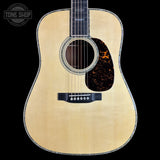 A front-facing acoustic guitar with a natural wood finish and a dark tortoiseshell pickguard, shown against a solid black background with a Tone Shop watermark in the top-left corner.