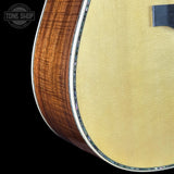 Close-up detail of an acoustic guitar body showing the natural wood side edge, the light yellow spruce top, and a decorative inlay along the edge, set against a black background with a Tone Shop watermark.