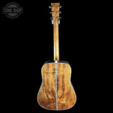 The back of an acoustic guitar with a highly figured wood top, showing prominent grain patterns and a glossy finish, photographed against a solid black background.