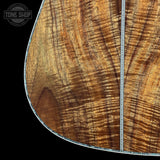 Close-up of a guitar body showing a rich, figured wood grain pattern in warm brown and golden tones, with a silver-toned edge trim and a vertical seam line, set against a solid black background.