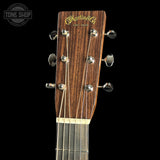 Close-up of the headstock of a Martin & Co acoustic guitar, showing the dark brown wood grain, gold script logo, and six silver tuning pegs against a solid black background.