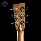 Close-up of the headstock of a wooden acoustic guitar against a solid black background, showing six tuning pegs and a Tone Shop watermark in the top left corner.