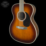 A close-up studio shot of an acoustic guitar body against a solid black background, featuring a classic sunburst finish that transitions from bright amber-orange in the center to dark brown at the edges. The guitar has a black pickguard, a silver-toned bridge, and white binding around the body.