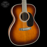 A classic acoustic guitar with a sunburst finish, featuring a warm orange-brown center fading to black around the edges, a black pickguard, and a silver-toned bridge, shown against a solid black background.