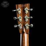 Close-up of a wooden guitar headstock with six silver tuning pegs and a dark brown wood grain finish, shown against a black background with a Tone Shop watermark in the top left.