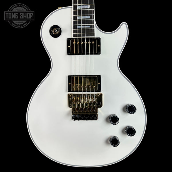 White electric guitar with a black pickguard on a black background, featuring the Tone Shop logo.