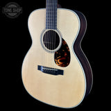 A close-up studio shot of an acoustic guitar body and upper neck against a black background, with a Tone Shop watermark in the top-left corner.