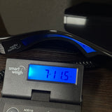 A close-up of a black digital smart scale with a blue backlit LCD display showing '7.115 lbs', with a black headband resting above it on a dark wooden surface.