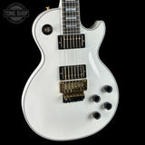 White electric guitar with a black pickguard on a black background, featuring the Tone Shop logo.