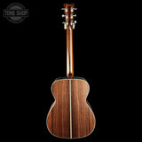 The back of an acoustic guitar with a rich brown wood grain finish, shown against a solid black background with a Tone Shop watermark in the top left corner.