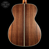 Close-up of the back of an acoustic guitar showing a rich, dark brown wood grain finish with a light cream center stripe and white edge binding, set against a solid black background.