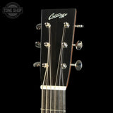 Close-up of the headstock of a Collings acoustic guitar against a black background, showing the brand name in white script and six tuning pegs.