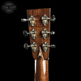Close-up of the headstock of an acoustic guitar, showing six tuning pegs with metallic silver and gold accents against a black background. A Tone Shop watermark is visible in the top left corner.