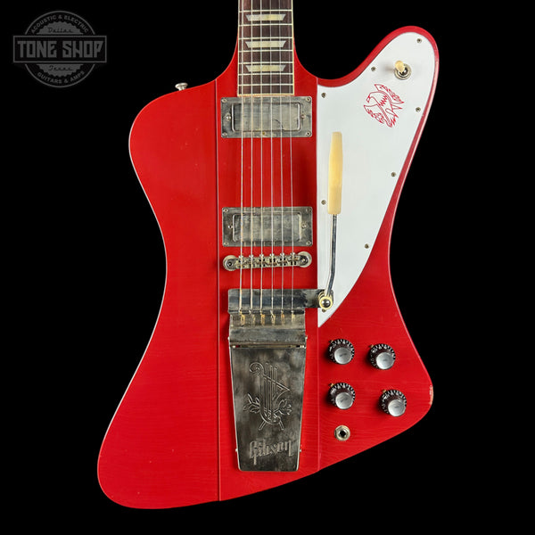 Red electric guitar with white pickguard on a black background, featuring the Gibson logo.