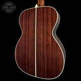 The back of an acoustic guitar with a rich dark brown wood grain finish, featuring a light-colored center stripe and white binding, shown against a solid black background.