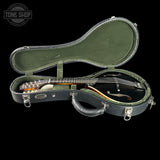 An open black mandolin case with an olive green felt interior, holding a black mandolin with a brown fingerboard, photographed on a black background. A Tone Shop logo watermark is visible in the top left corner.