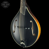 A close-up studio shot of a mandolin against a solid black background, featuring a glossy black body with a light wood edge, gold-toned f-holes, and a dark neck.