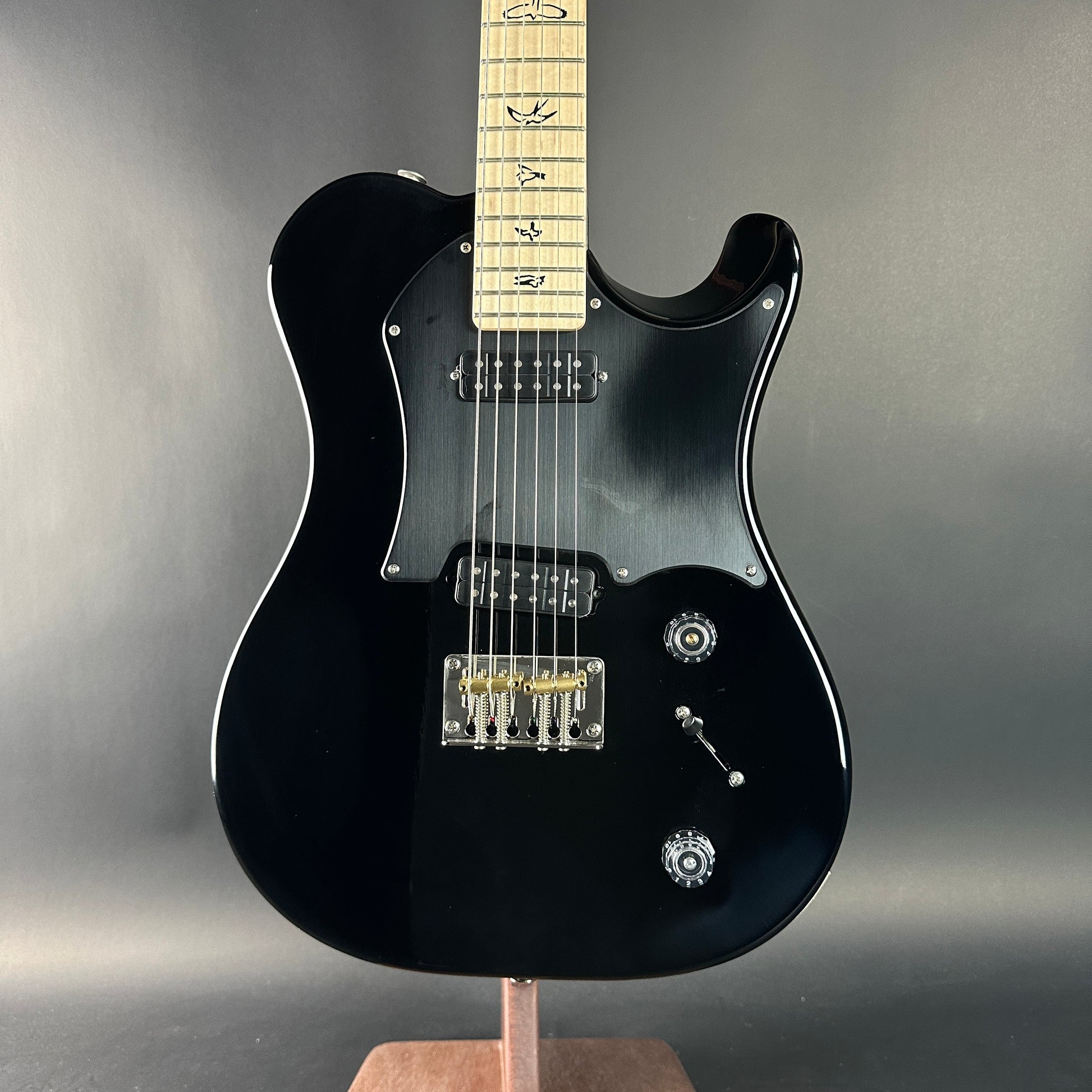 Black electric guitar on a stand against a gray background