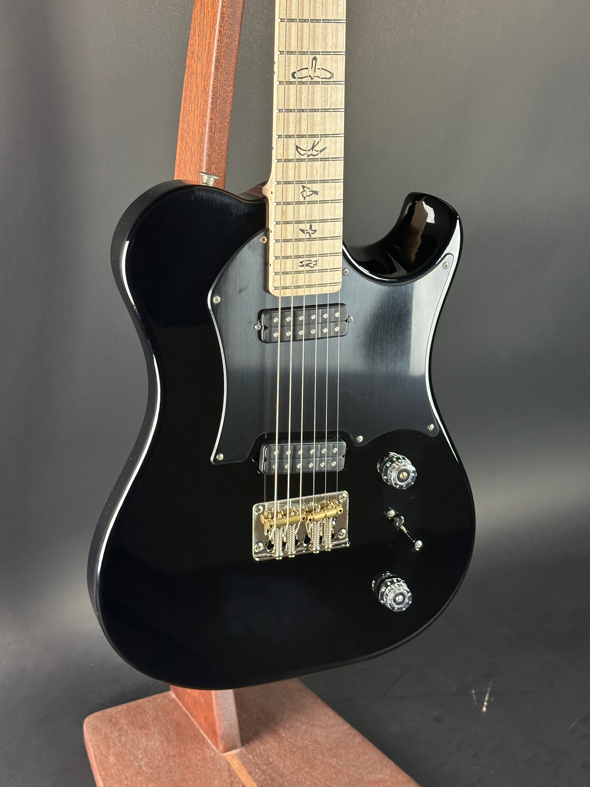 Black electric guitar with a wooden fretboard on a dark surface