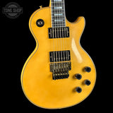 Yellow electric guitar with a black pickguard on a black background, featuring 'Tone Shop' branding.