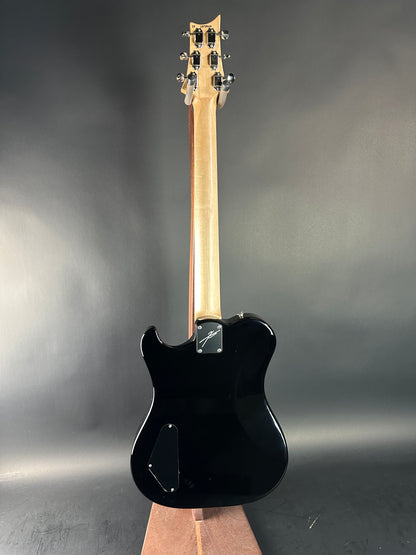 Black electric guitar with a wooden neck on a dark gray background