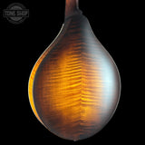 Close-up of the back of a mandolin with a teardrop-shaped body, showing a rich warm brown wood grain finish against a black background. A Tone Shop watermark is visible in the top-left corner.