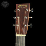 Close-up of the headstock of a Martin & Co acoustic guitar, showing the dark brown wood grain, gold script logo, and six silver tuning pegs against a black background.