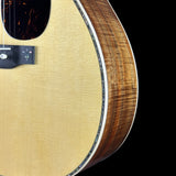 Close-up of an acoustic guitar body showing the natural wood grain top, soundhole surround, and side edge against a black background.