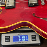 Red electric guitar on a digital scale displaying weight